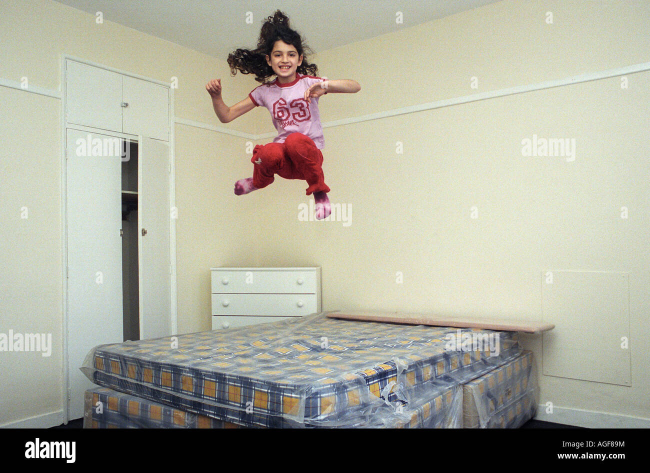 Una giovane ragazza di età compresa tra i 9, salta su un letto in una stanza vuota. Foto Stock