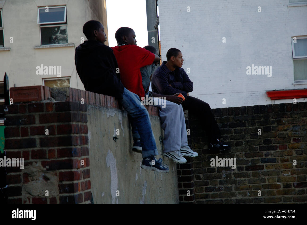 Giovani ragazzi al di fuori della scuola e la noia alimentato fino seduti sulla parete in Brixton a sud di Londra in attesa. Foto Stock