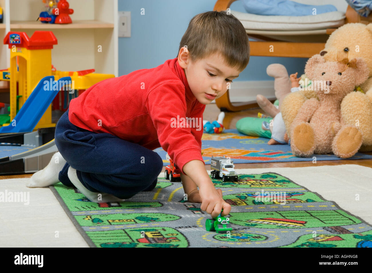 Tre anni di vecchio ragazzo gioca con automobili giocattolo sul tappeto con strade e case su di esso Foto Stock