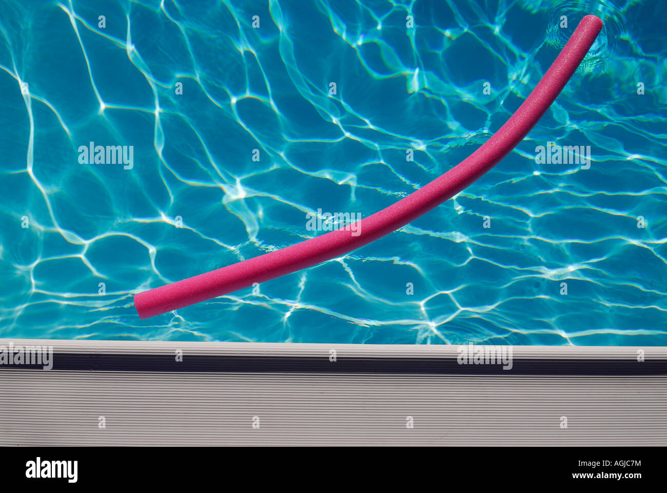 Piscina rosa a base di noodle flottante in una piscina blu con luce rifratta sul fondo e bordo bianco abstract Foto Stock