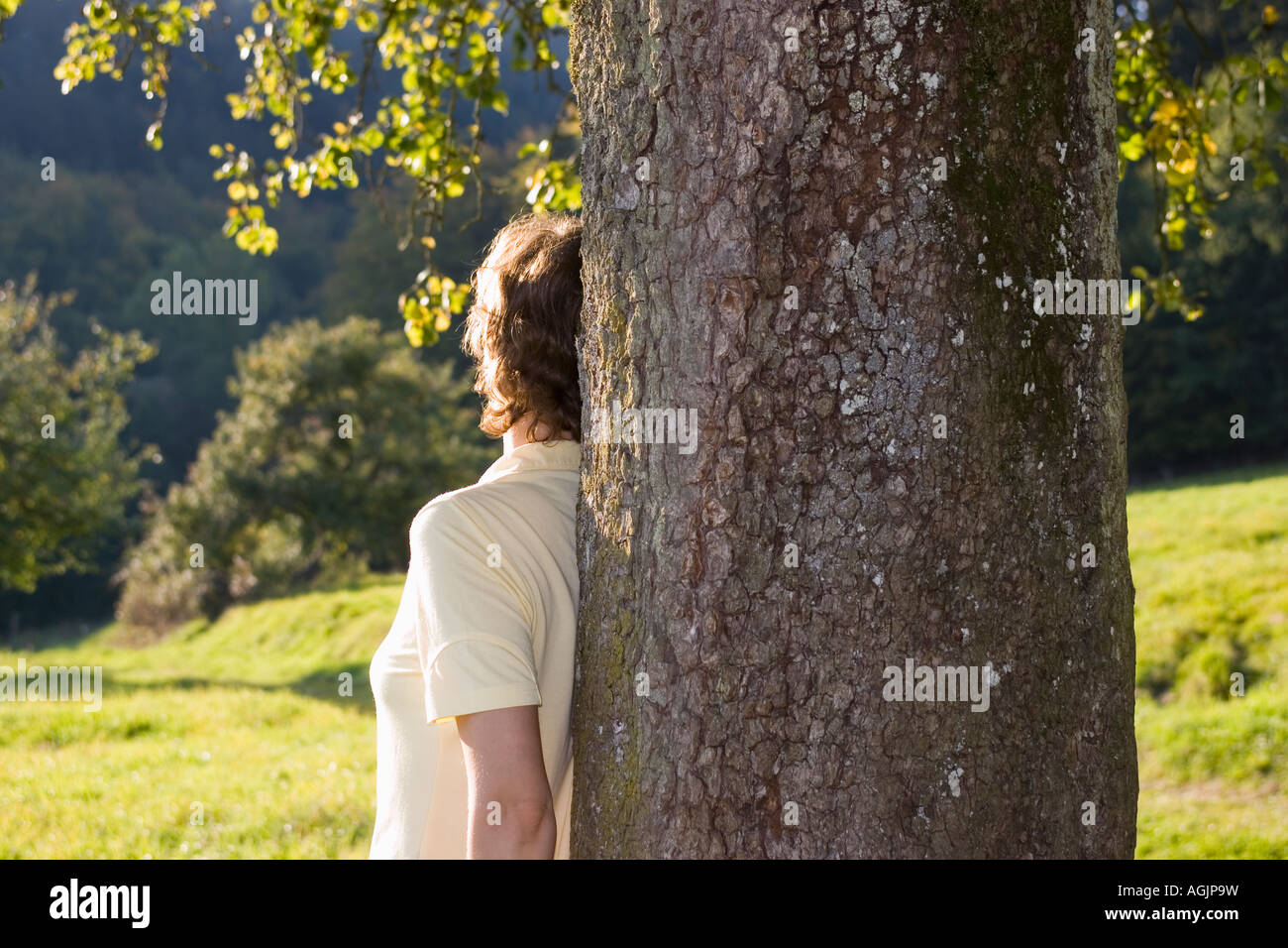 Donna appoggiata ad un albero al tramonto Foto Stock