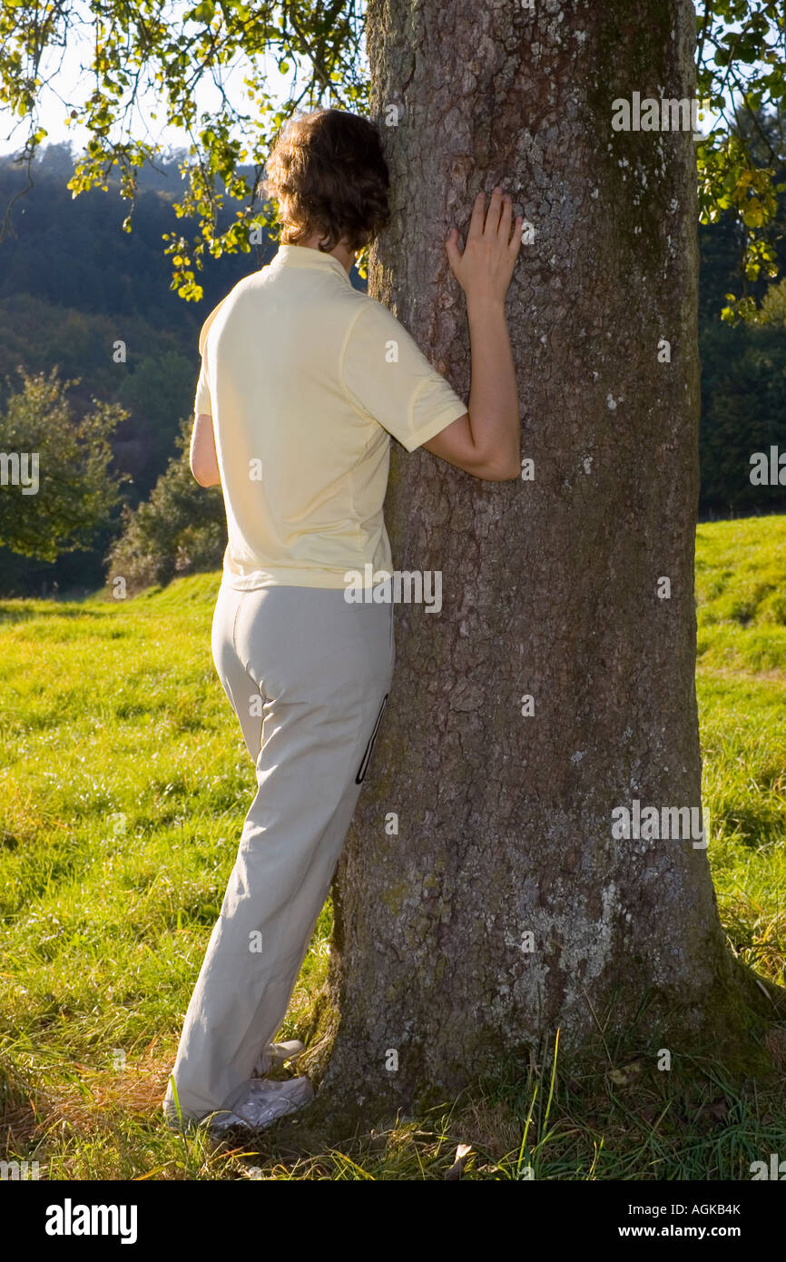 Donna appoggiata ad un albero in un prato Foto Stock