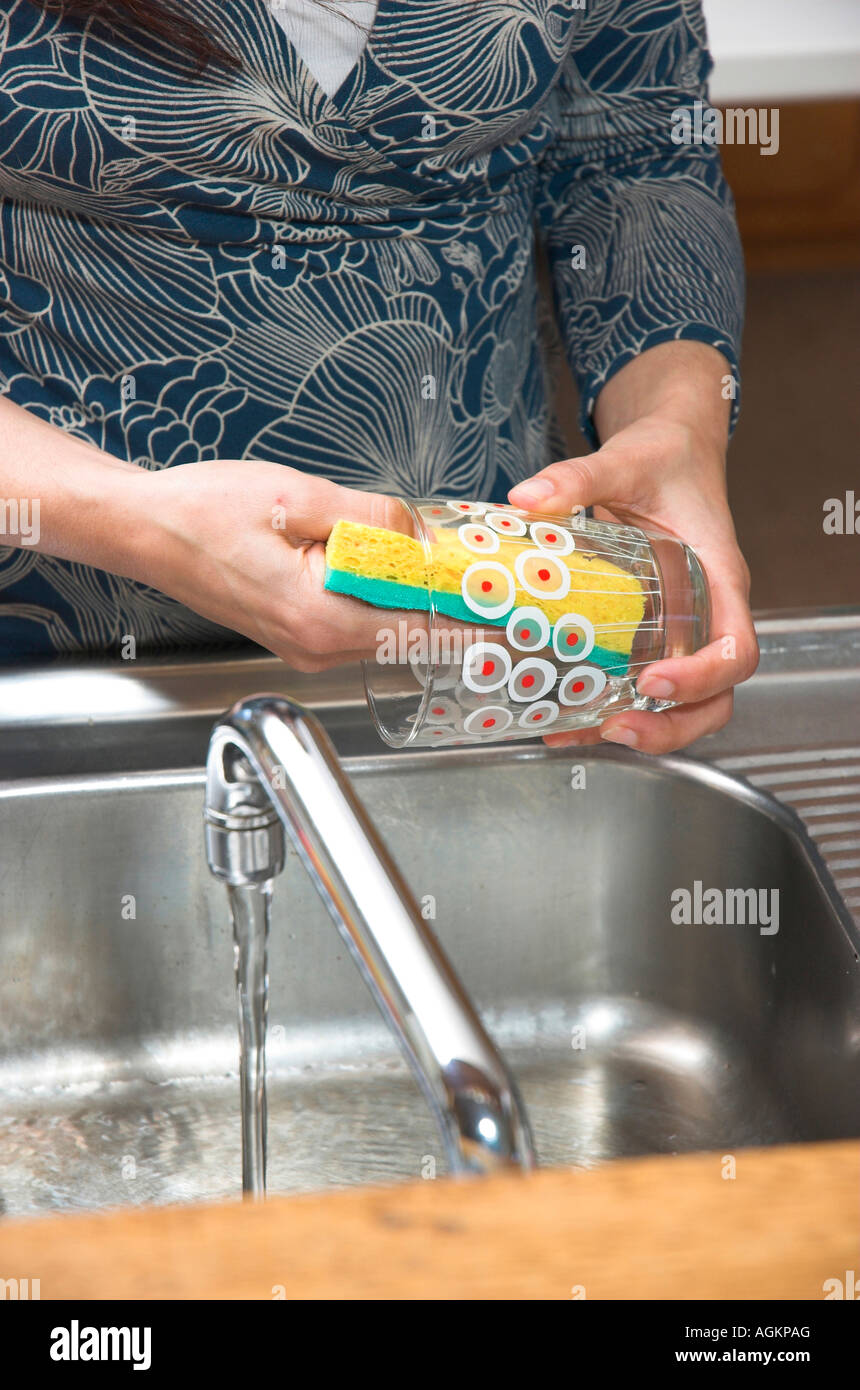 Donna di lavaggio di un vetro al lavello da cucina mentre l'acqua scorre dal rubinetto Foto Stock