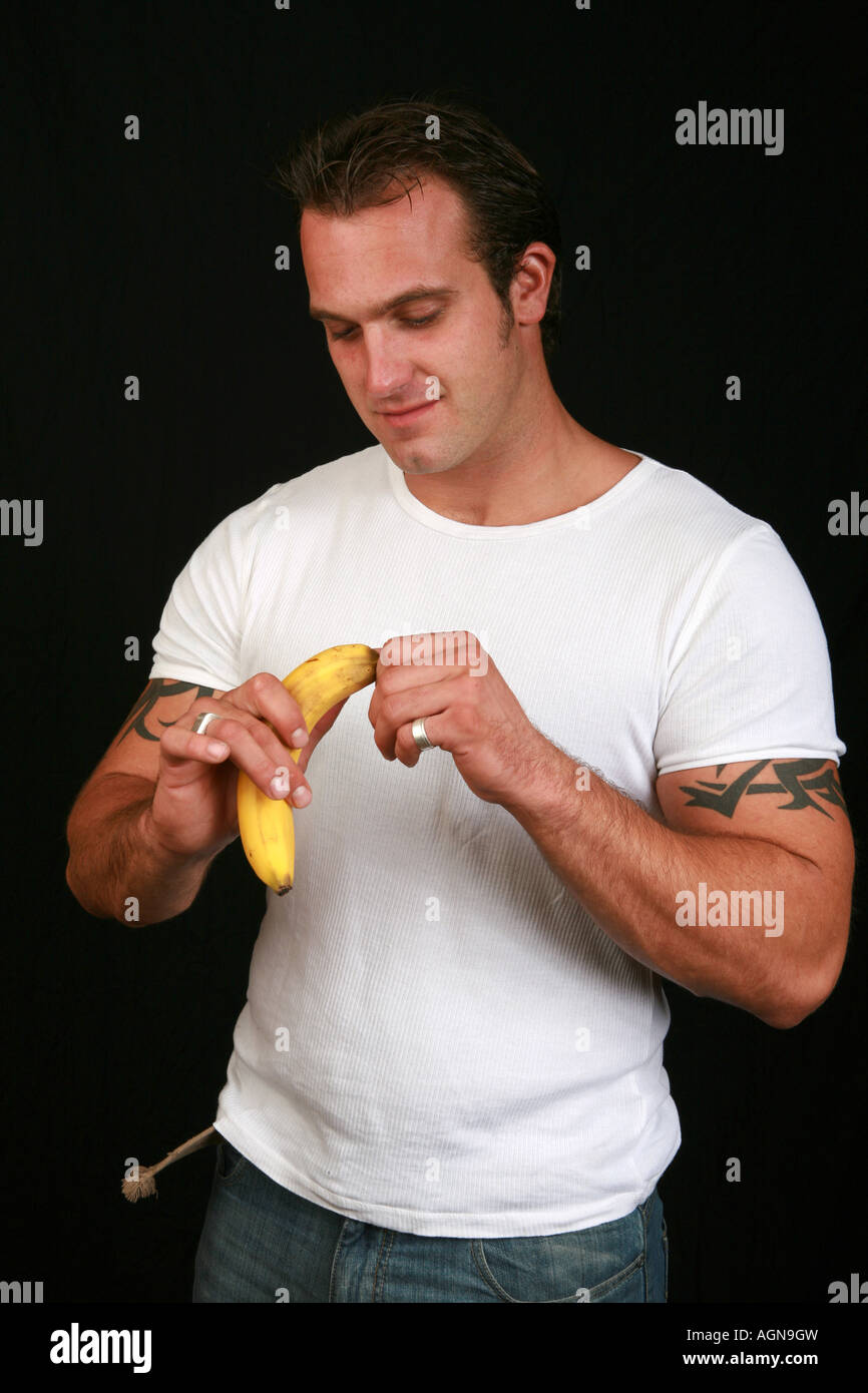 Un mangiare sano giovane muscolare bello 20s maschile in bianco t shirt bucce di banana un pezzo di frutta prima di mangiare snack sani Foto Stock