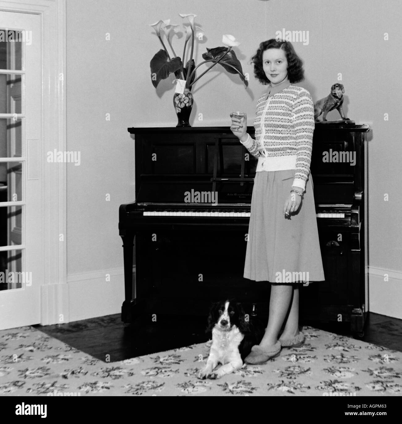 Vecchia famiglia vintage fotografia istantanea della giovane donna con drink IN PIEDI NELLA PARTE ANTERIORE DEL PIANO CON IL CANE del 1950 circa Foto Stock