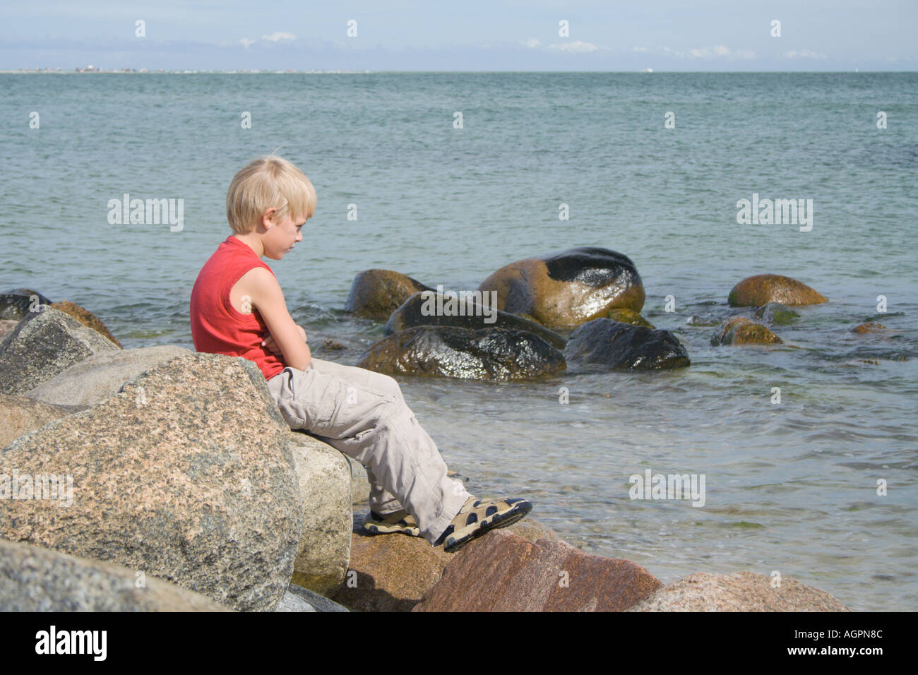 Ragazzo seduto sulle rocce in riflessione umore bracci ripiegati a Skagen nello Jutland in Danimarca Foto Stock