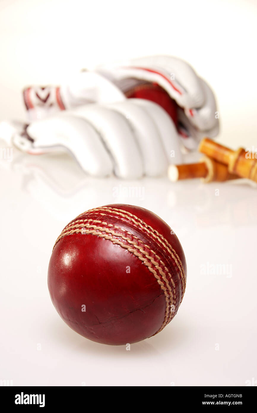 Sfera di cricket uno rosso marrone rossiccio rotondo con due guanti una coppia e due bails ligneo in background sul coperchio bianco India verticale Foto Stock