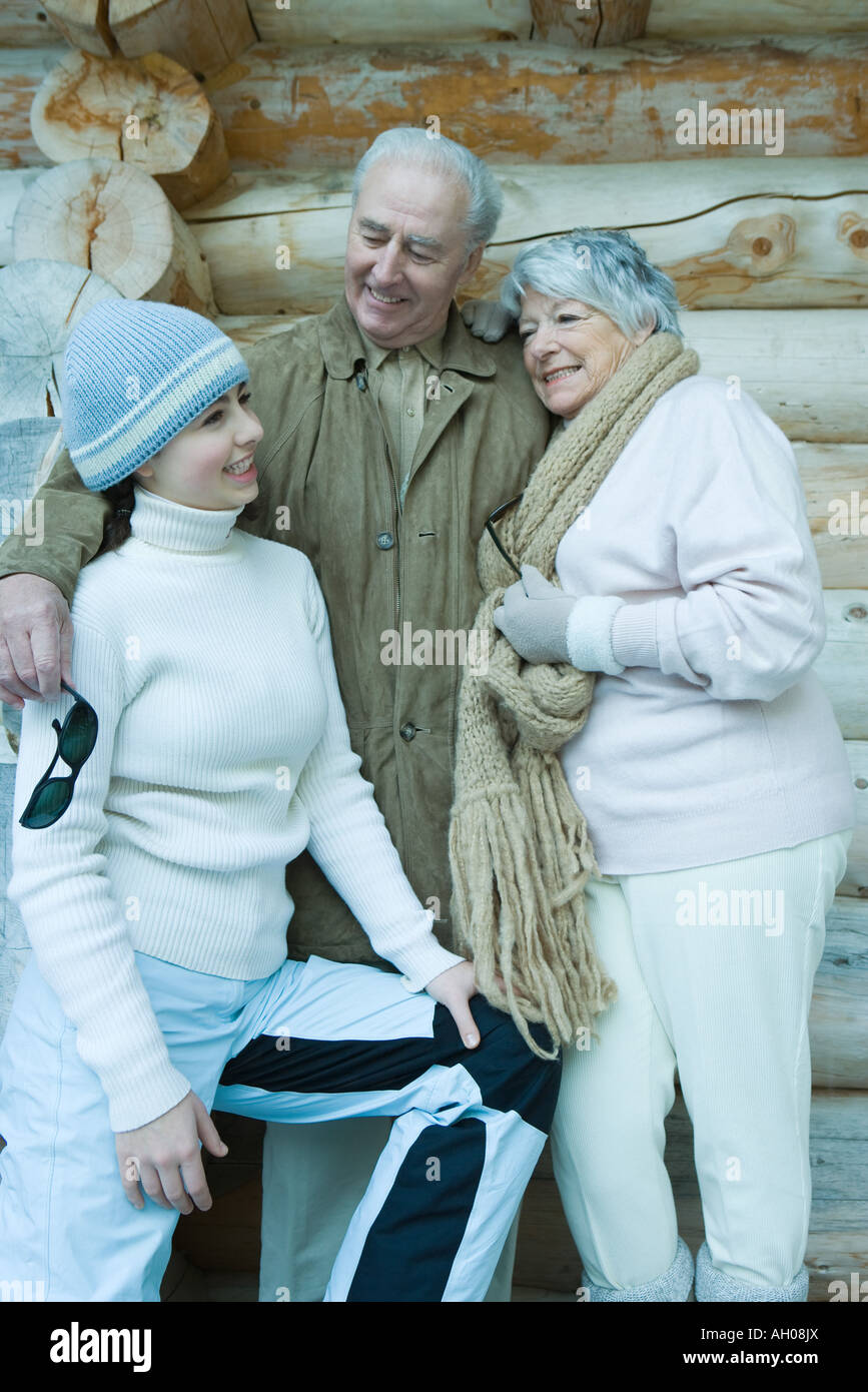 Teen ragazza con i nonni, indossare abbigliamento invernale, in piedi di fronte a log cabin, ritratto Foto Stock