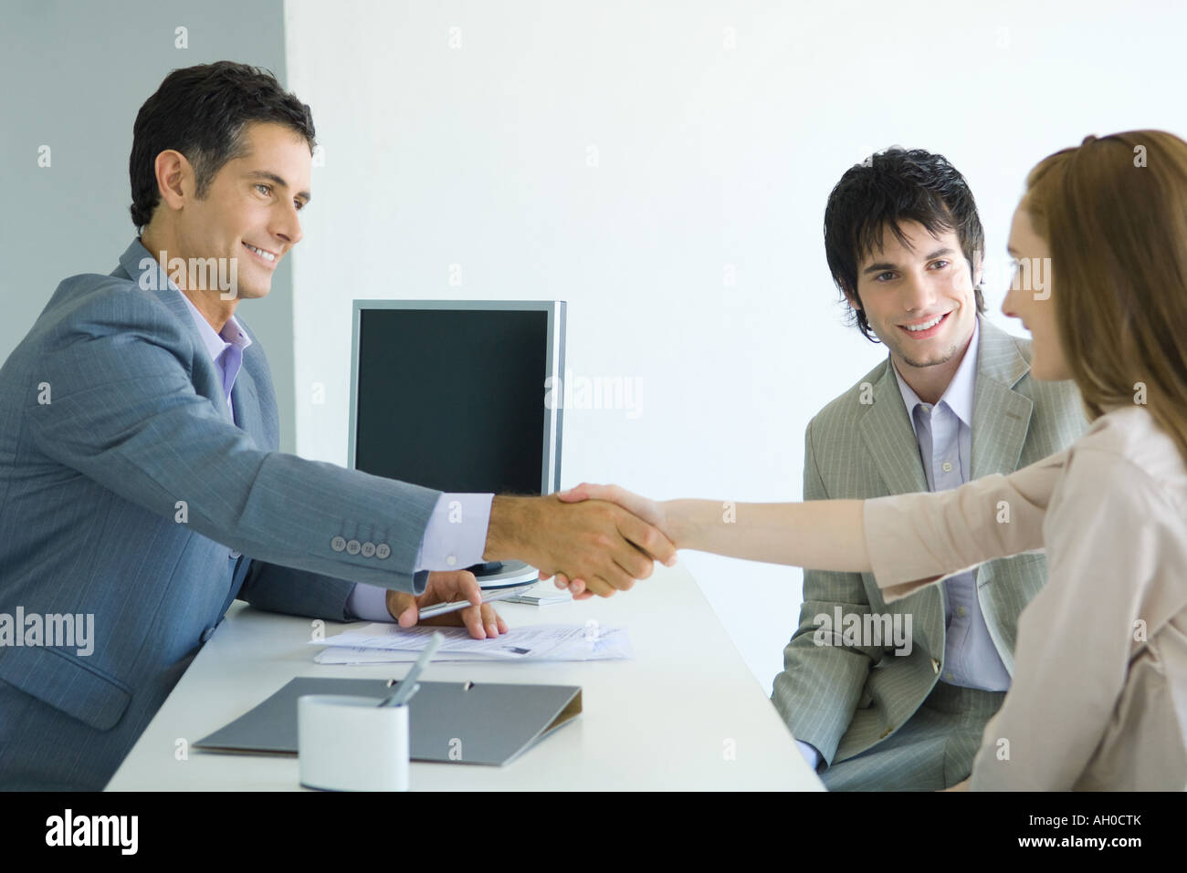Imprenditore stringono le mani con la giovane donna di fronte desk, giovane donna compagno maschio sorridente Foto Stock