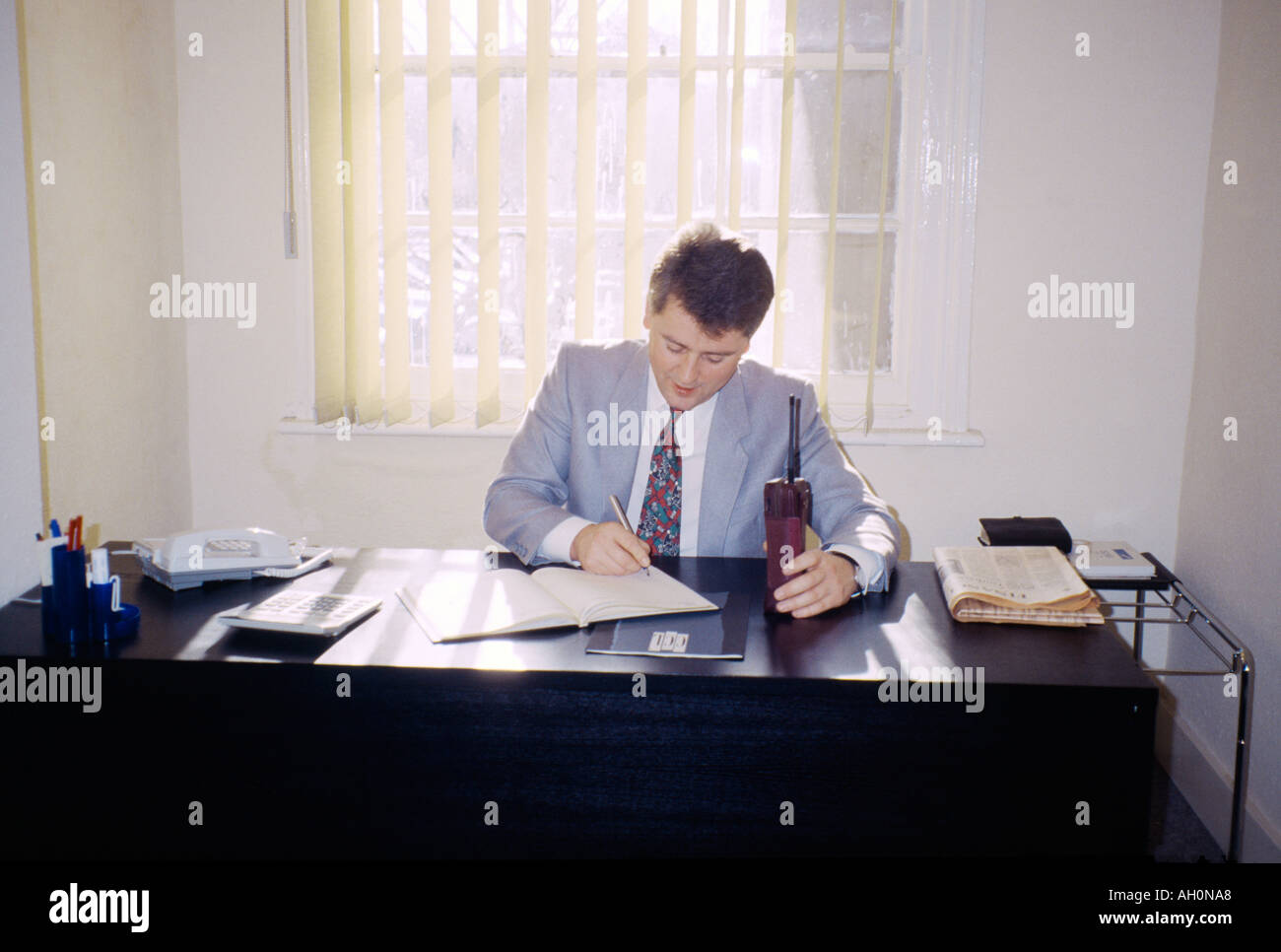 Uomo alla scrivania con il vecchio telefono cellulare Foto Stock