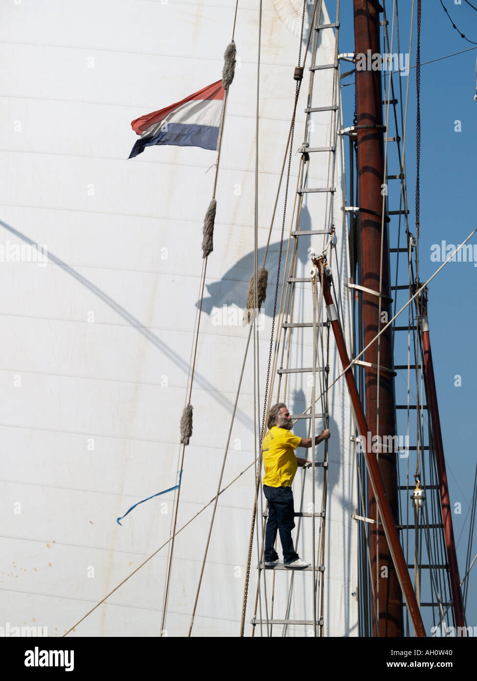 Barbuto marinaio di la goletta Bel Espoir II inviato aloft con vela e bandiera olandese in background girato a vela Amsterdam 2005 Foto Stock