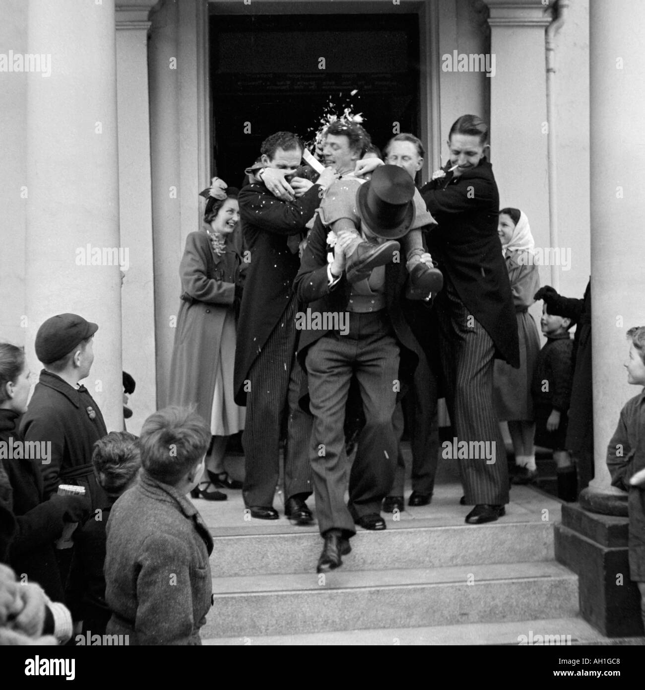 Vecchio VINTAGE IN BIANCO E NERO DI FAMIGLIA fotografia istantanea dello sposo essendo portati dalla cerimonia di nozze da ospiti di sesso maschile Foto Stock