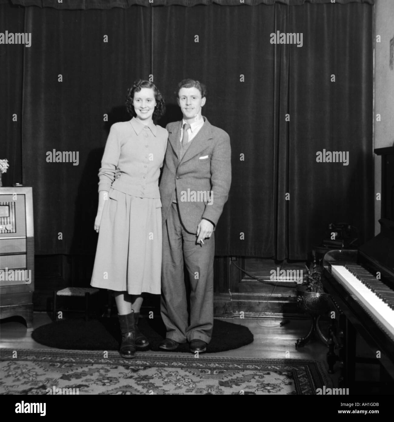 Vecchia famiglia VINTAGE FOTOGRAFIA SNAP SHOT COPPIA SPOSATA IN PIEDI IN SALOTTO con il pianoforte e la vecchia radio del 1950 circa Foto Stock