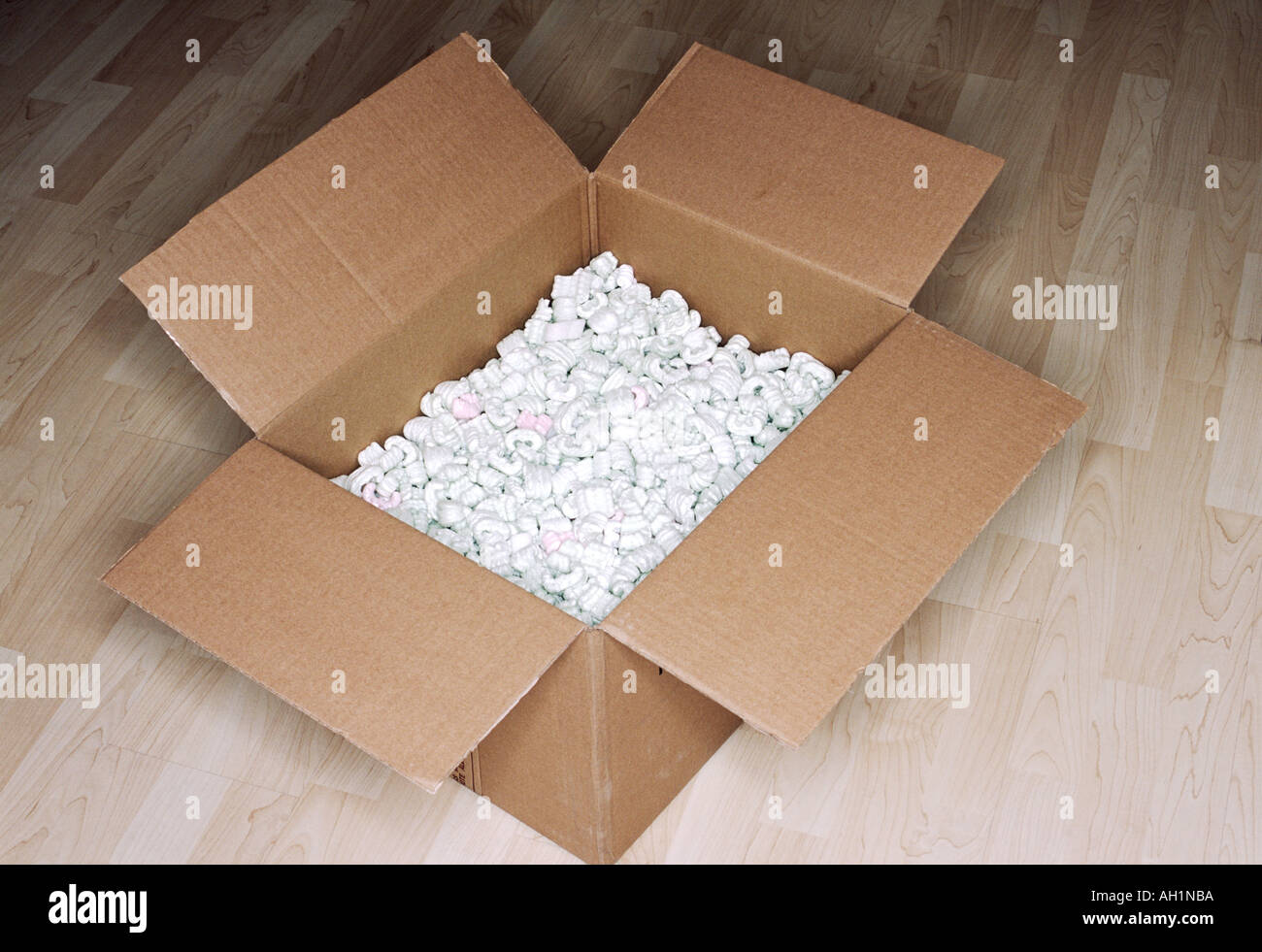 Una guarnizione scatola di cartone aperto e pieno di luce Styrofoam di imballaggio di plastica all'interno di fagioli su legno luce pavimento in legno ancora vita Foto Stock