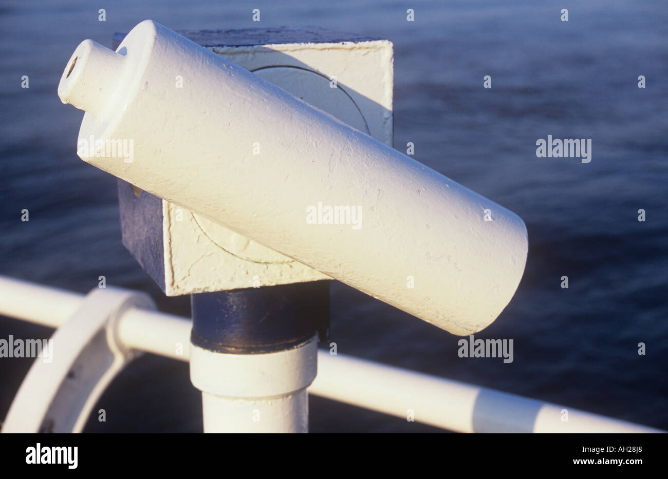 Close up di un telescopio di mare accanto alle ringhiere in bianco che si affaccia su un mare di rigonfiamento nella luce calda del sole Foto Stock