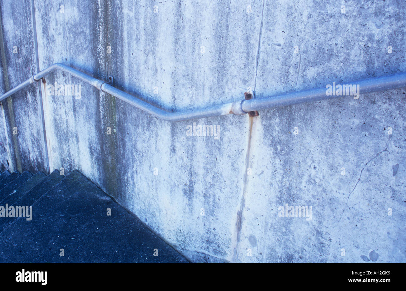 Parte di un volo di passi concreti affiancato da un macchiato e weathered muro di cemento con corrimano in alluminio Foto Stock