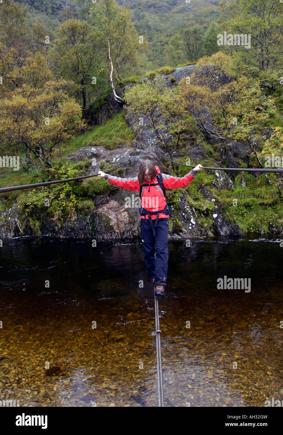 Trekker femmina attraversando un ponte sospeso in Glen Nevis Scozia Scotland Foto Stock