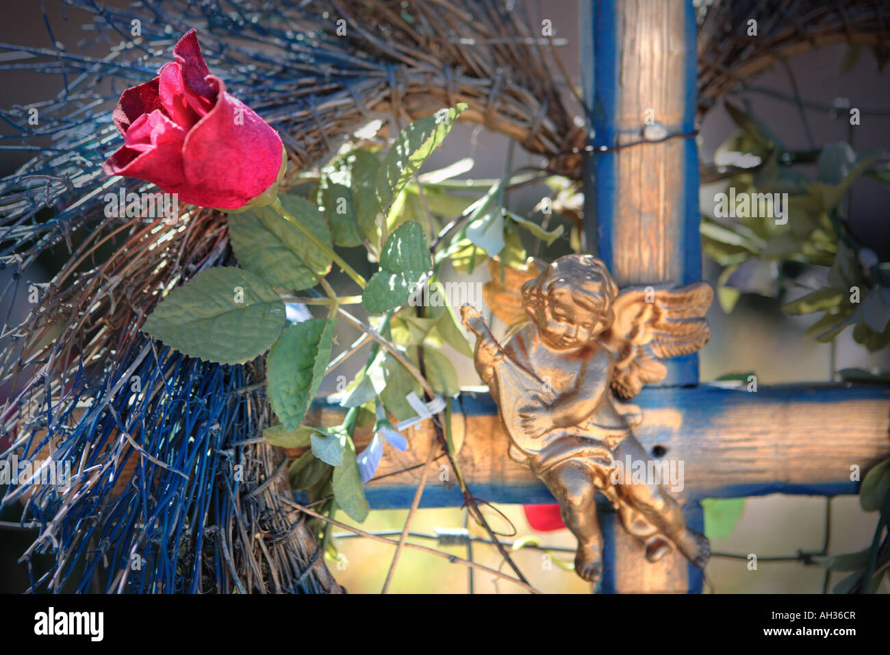 Croce di legno adornati con fiori artificiali e cherubino figurina Foto Stock