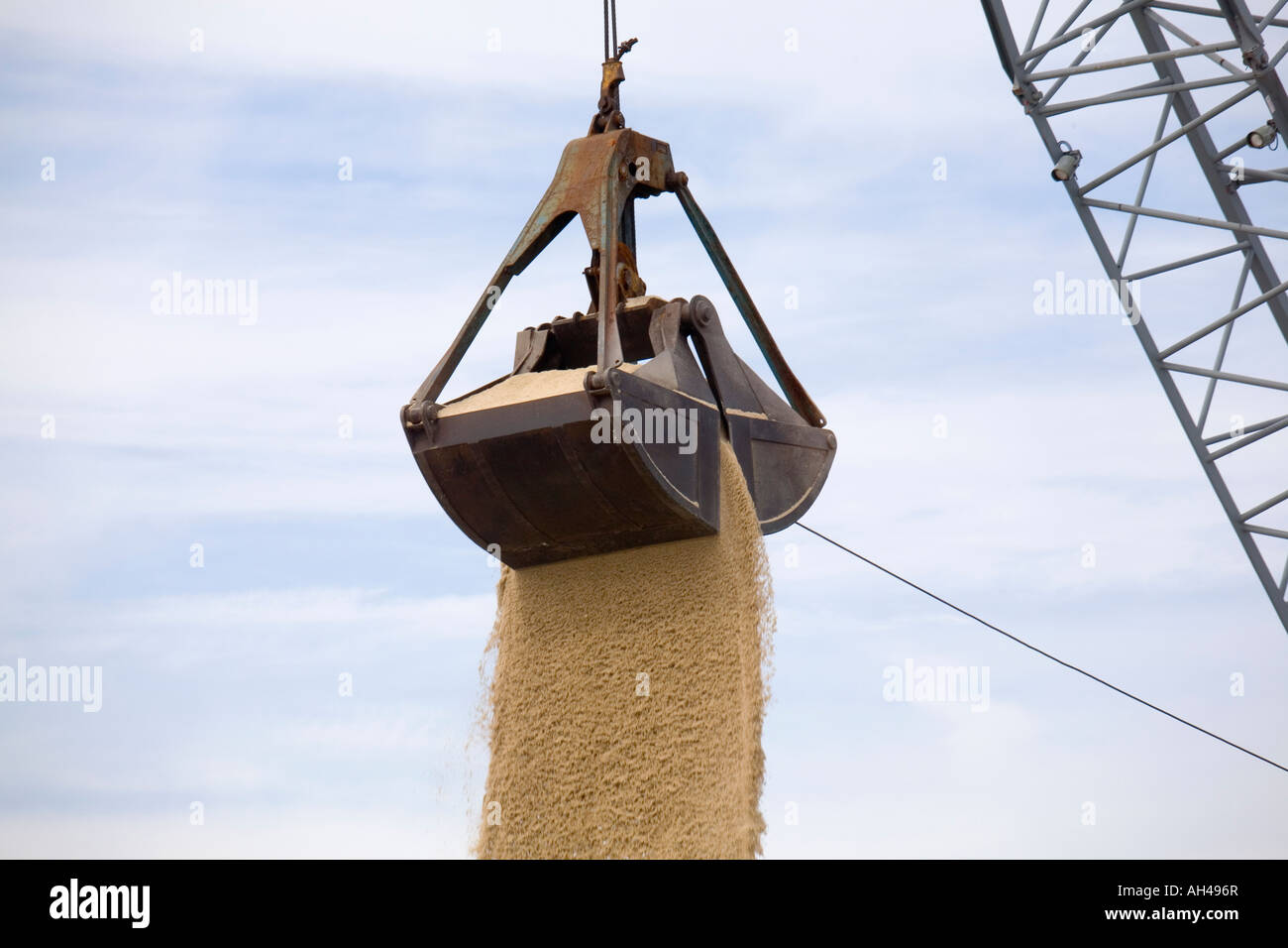 Una benna bucketloader alleggerimento del carico di sabbia da una petroliera in attesa di una nave. Foto Stock