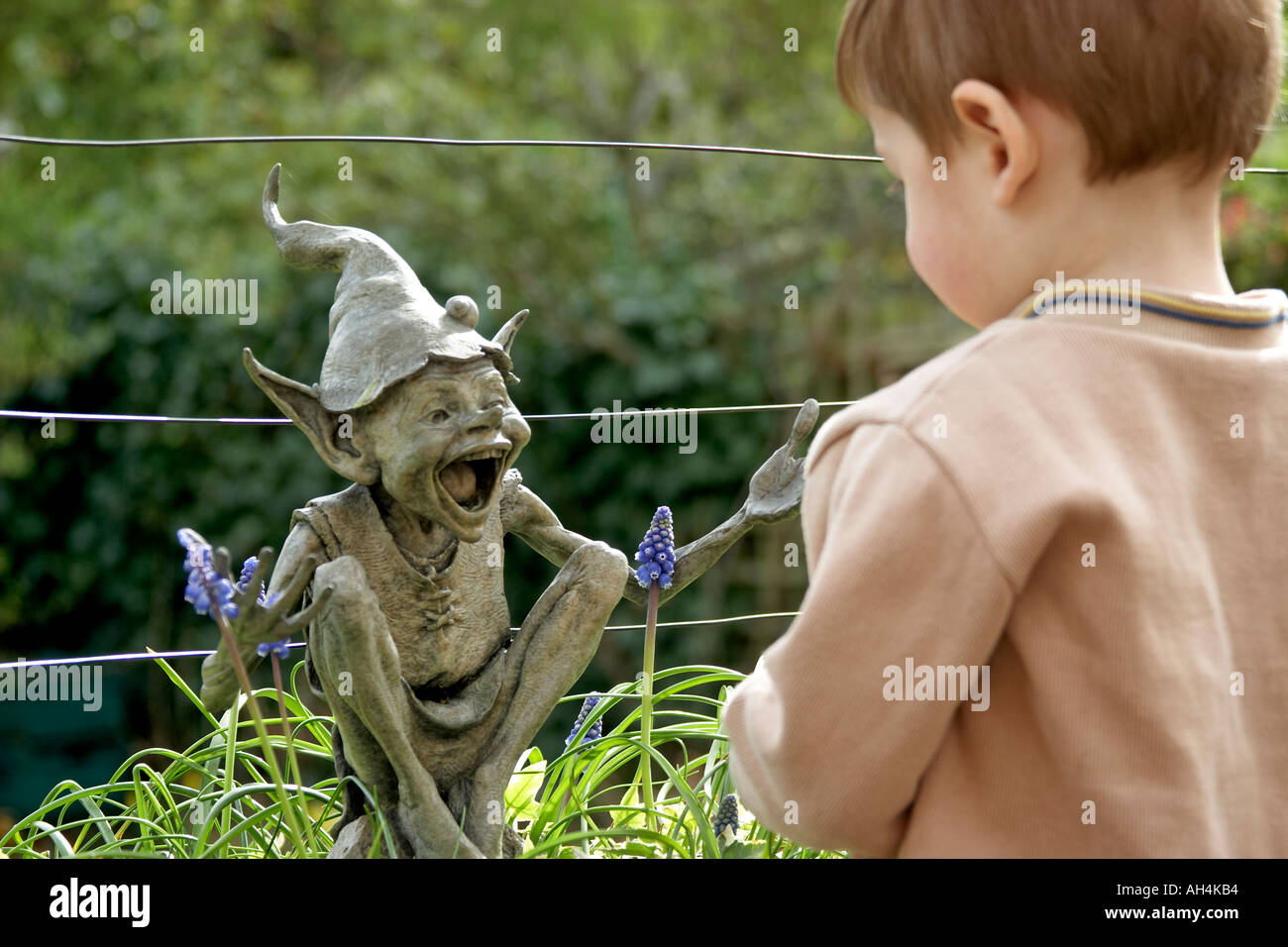 Attraente giovane ragazzo bambino in un giardino suburbano in primavera la riproduzione con un Elfo scultura di David Goode e uva CJWH giacinto Foto Stock