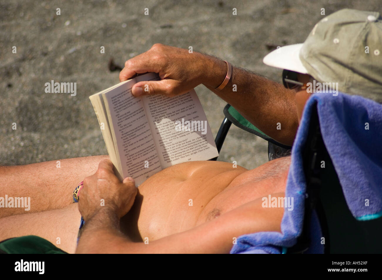 Uomo di mezza età a prendere il sole sulla spiaggia e la lettura di un romanzo in brossura, aberystwyth ceredigion nel Galles Foto Stock