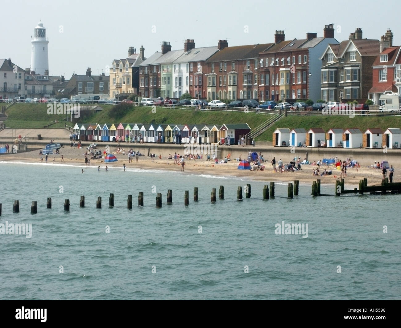 Caldo giorno estivo del sud, affollato dai visitatori accanto alle capanne sulla spiaggia del Mare del Nord, edifici fronte mare e faro Suffolk East Anglia Inghilterra, Regno Unito Foto Stock