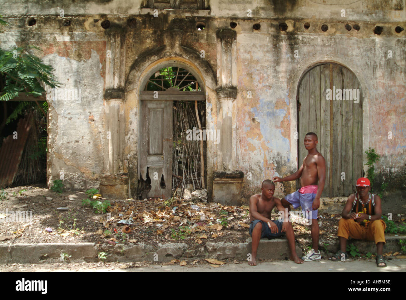 Un uomo avente il suo taglio di capelli di fronte un decadimento portoghese edificio coloniale sulle strade di Ibo Island. Mozambico, Africa Foto Stock