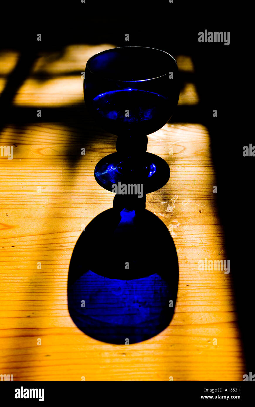 Un vetro di colore blu e la sua ombra su una tavola di pino Foto Stock