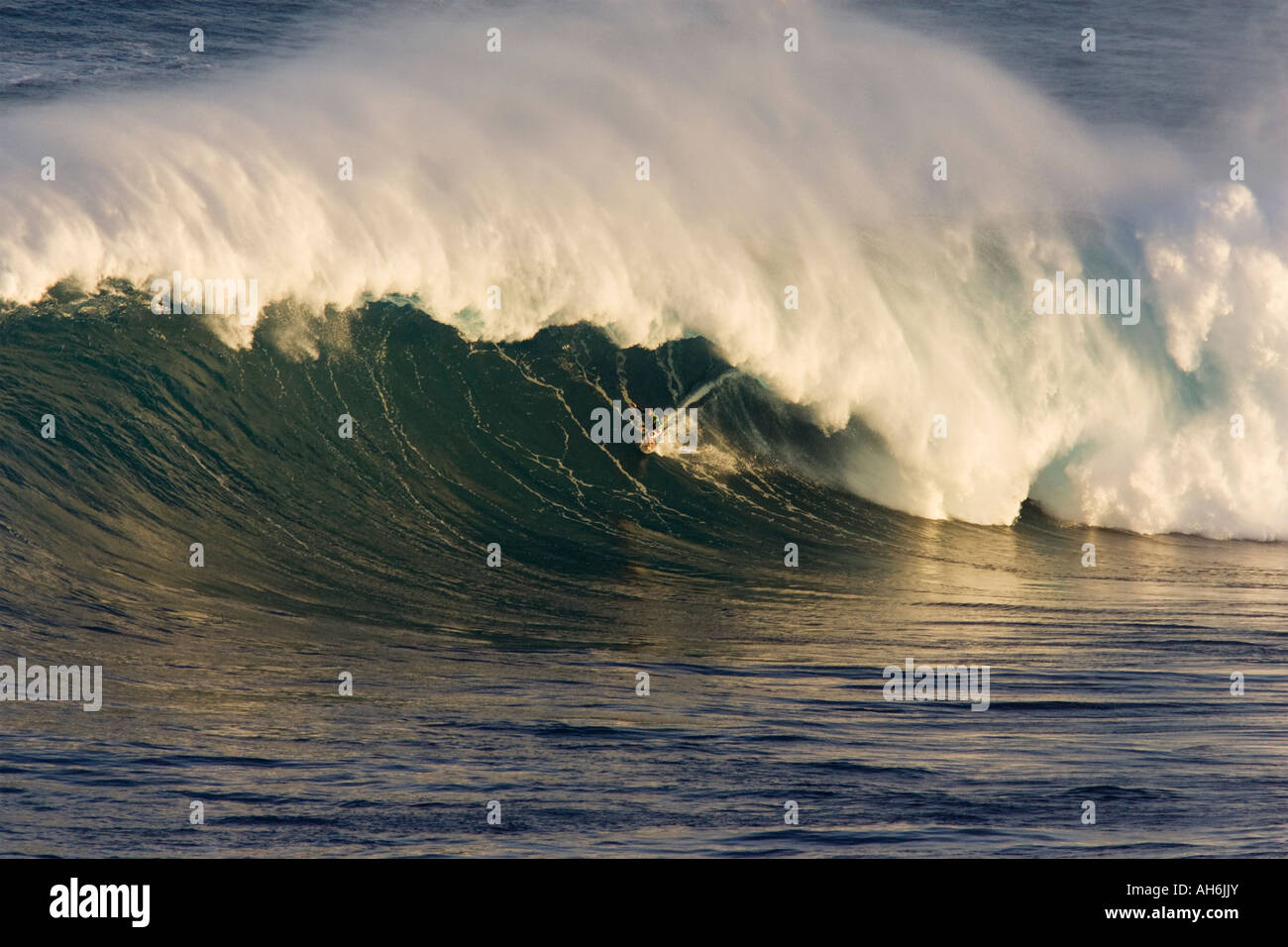 Un surfista cavalca un grande onda con spray offshore a ganasce, Maui. Foto Stock
