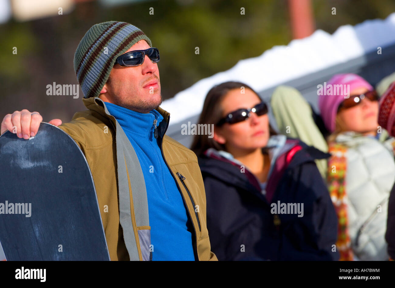 Metà uomo adulto tenendo un snowboard con due donne dietro di lui Foto Stock