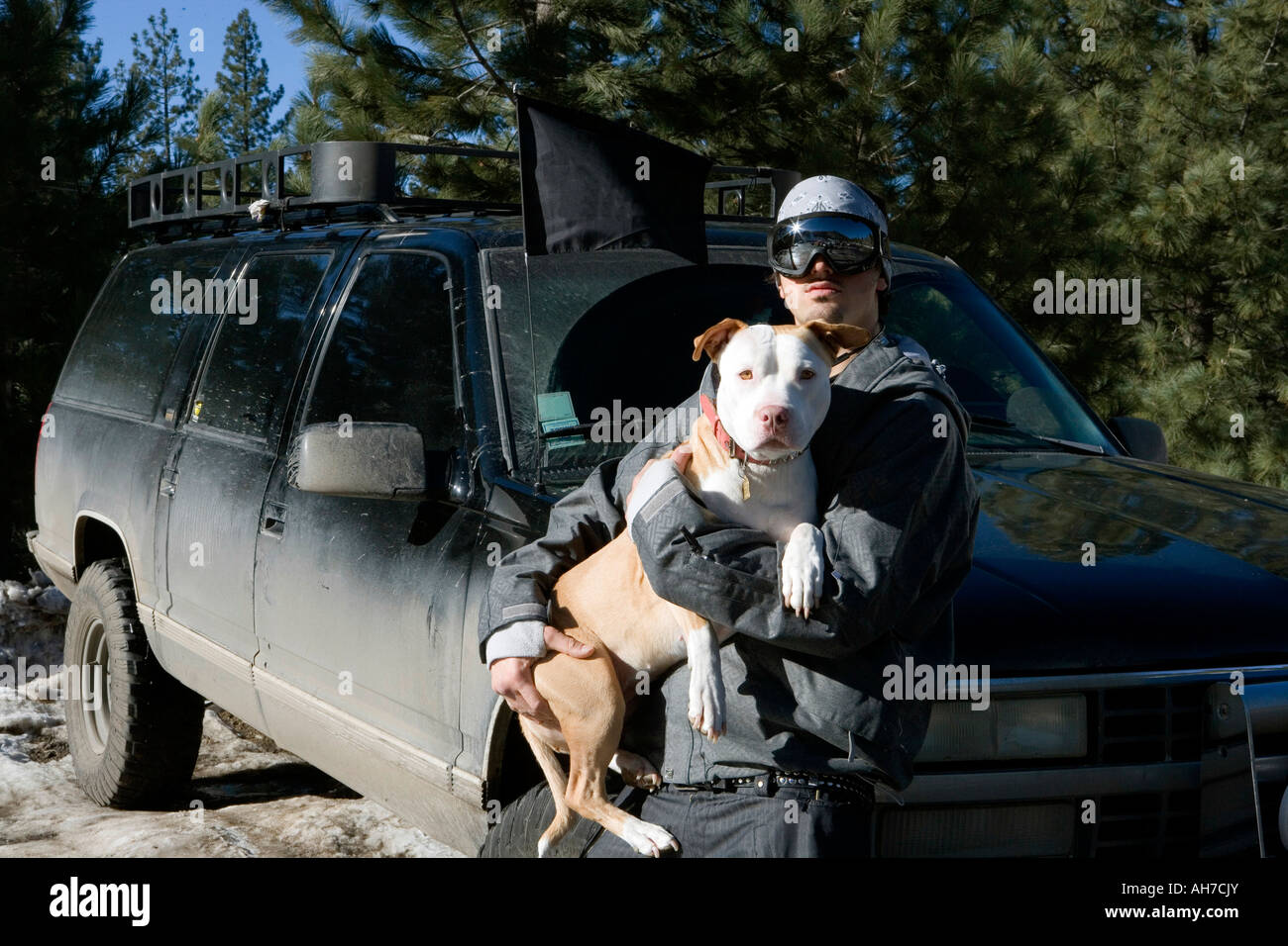 Giovane uomo adulto tenendo un cane accanto a uno sport utility vehicle Foto Stock