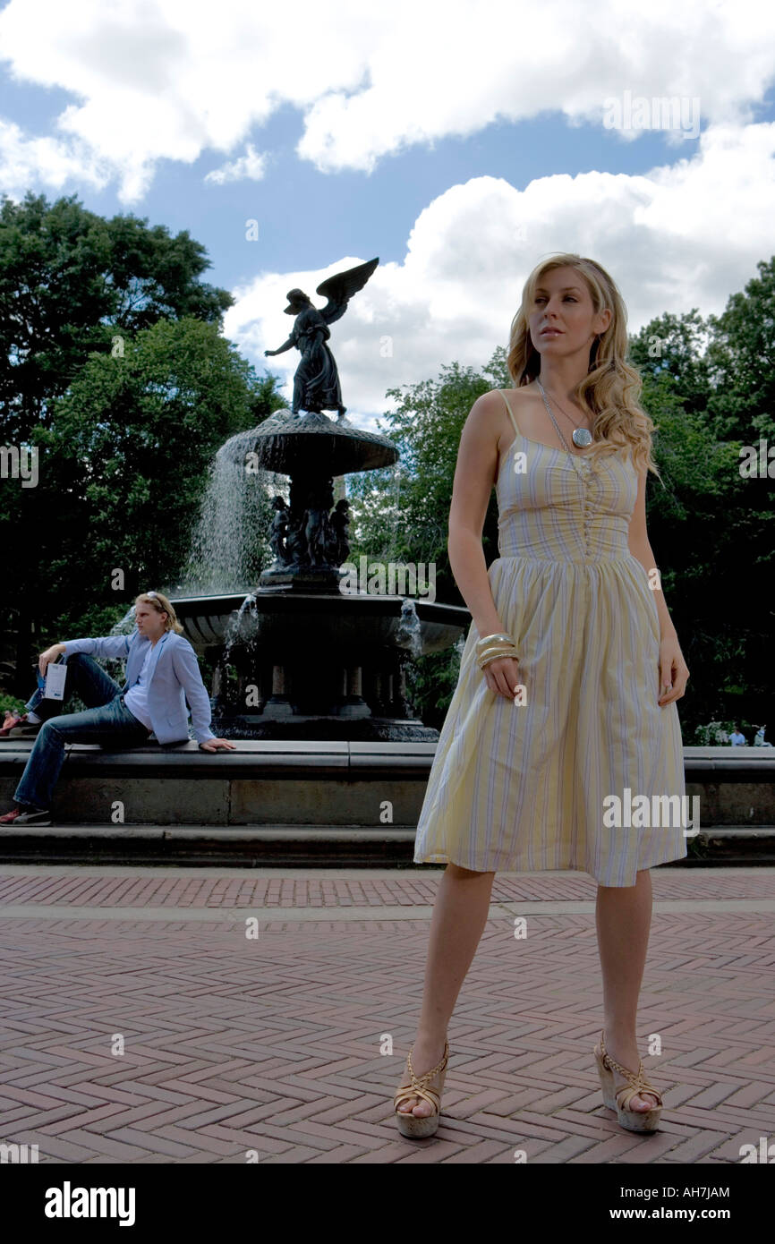 Giovane donna in piedi su un percorso con un giovane uomo seduto in background nei pressi di una fontana, Central Park, Manhattan, New York Cit Foto Stock