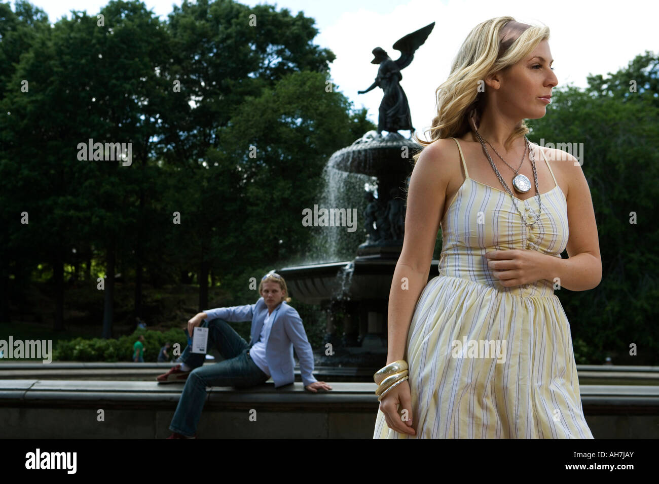 Giovane donna in piedi con un giovane uomo seduto in background, Central Park, Manhattan, New York, New York, Stati Uniti d'America Foto Stock