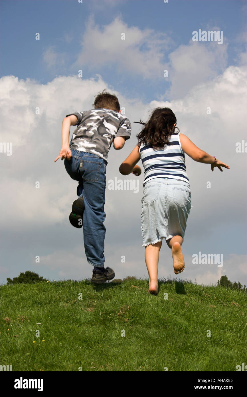 Dieci anni di un ragazzo e una ragazza correre e saltare fino a banca erbosa. Foto Stock