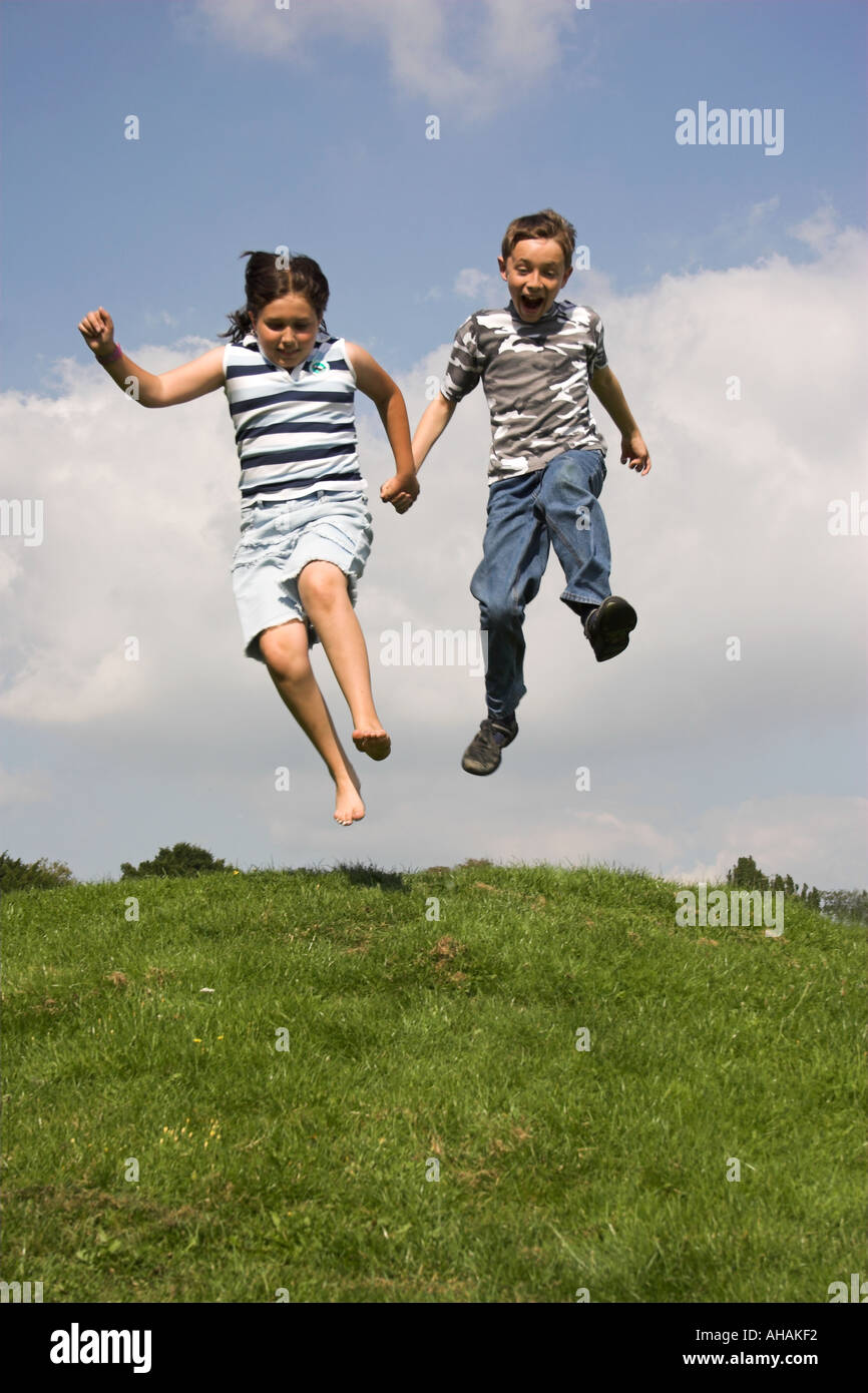 Dieci anni di un ragazzo e una ragazza correre e saltare giù una banca erbosa. Foto Stock