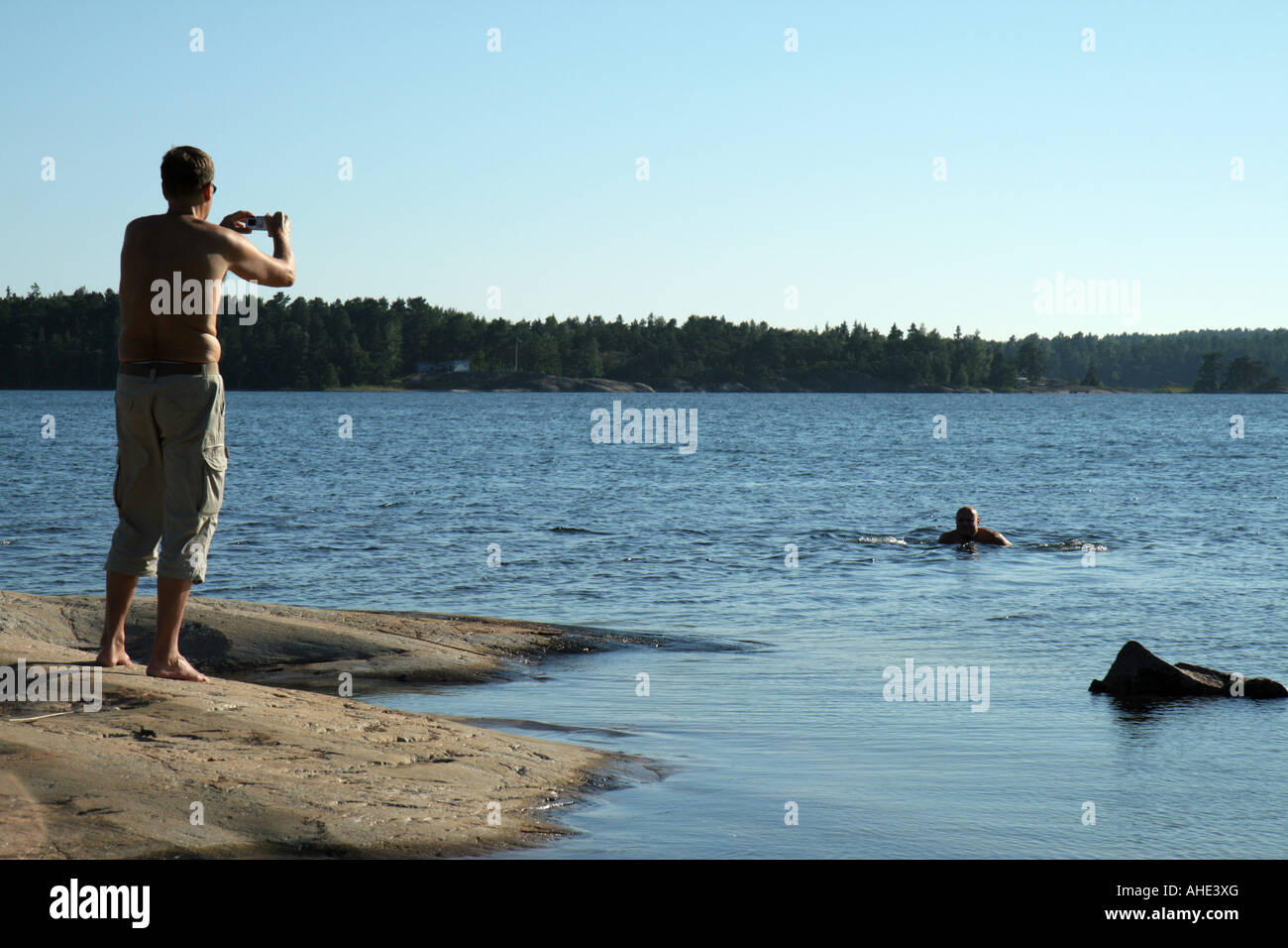 Uomo con una fotocamera digitale compatta di scattare una foto di un suo amico nuotare nel mare dell'arcipelago svedese Foto Stock