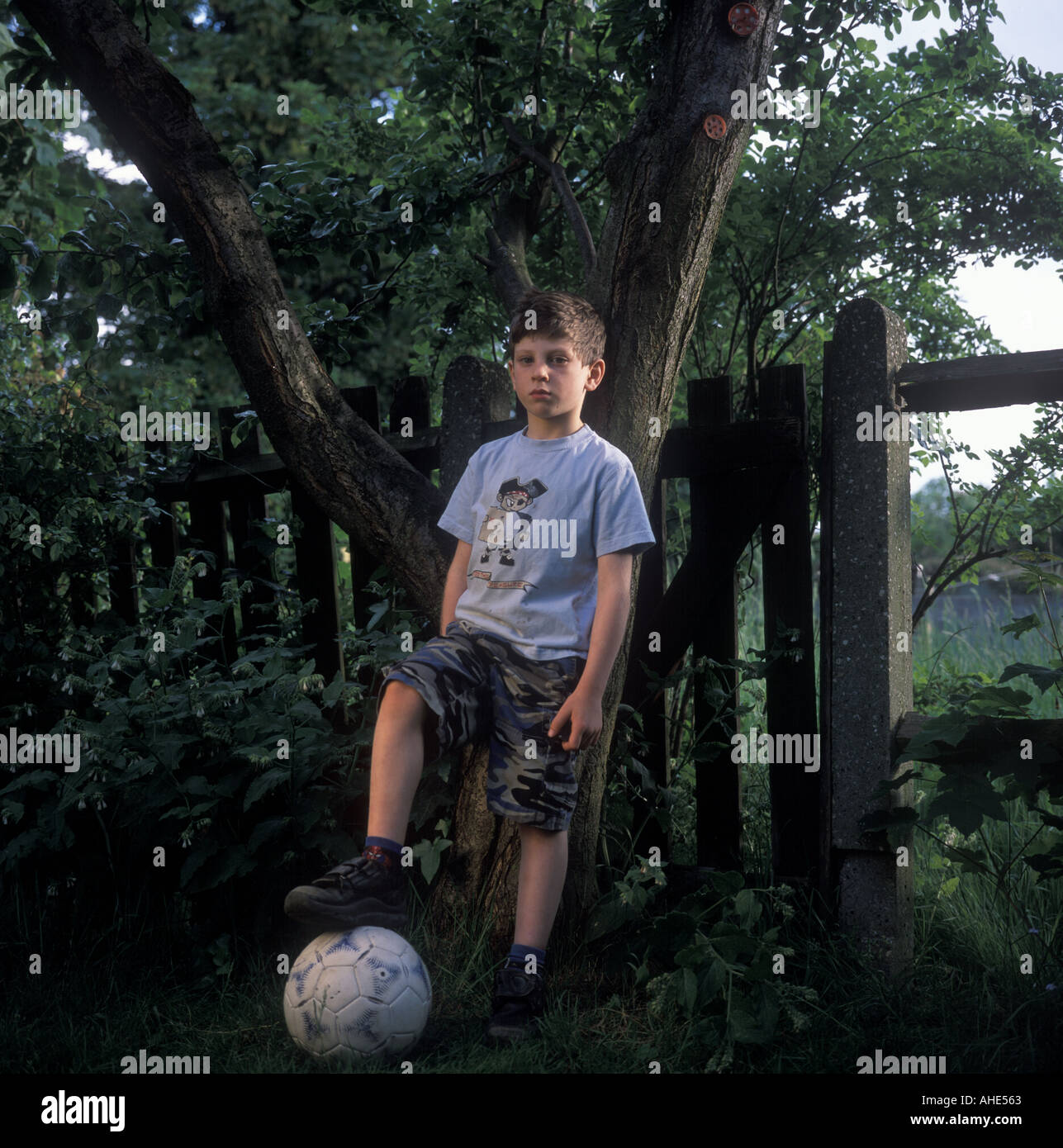 Un bambino di sei anni ragazzo sta con il suo calcio nei suoi genitori garden, Londra, Regno Unito. Foto Stock