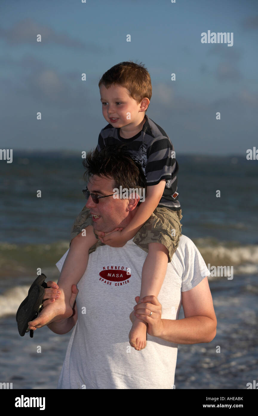 Metà degli anni trenta papà indossando occhiali da sole che porta tre enne figlio sulle sue spalle mentre passeggiate sulla spiaggia nella contea di Wexford Foto Stock