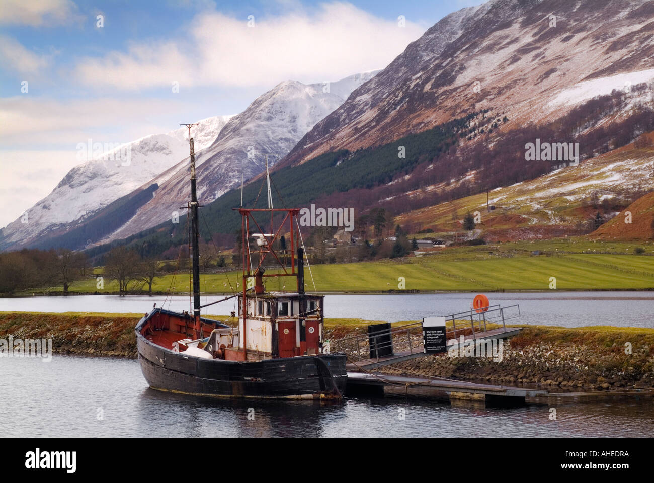 Un paesaggio scozzese shot in inverno con montagne innevate con un peschereccio ormeggiato a lochside Foto Stock