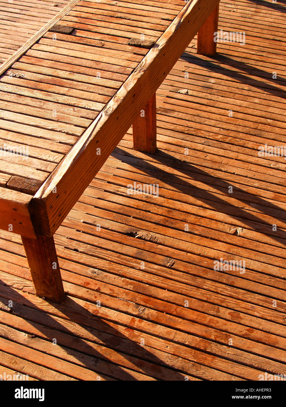 Lunga panca di legno che si elevano da una lunga planked pavimento in legno nel pomeriggio, mostra ombre lunghe Foto Stock