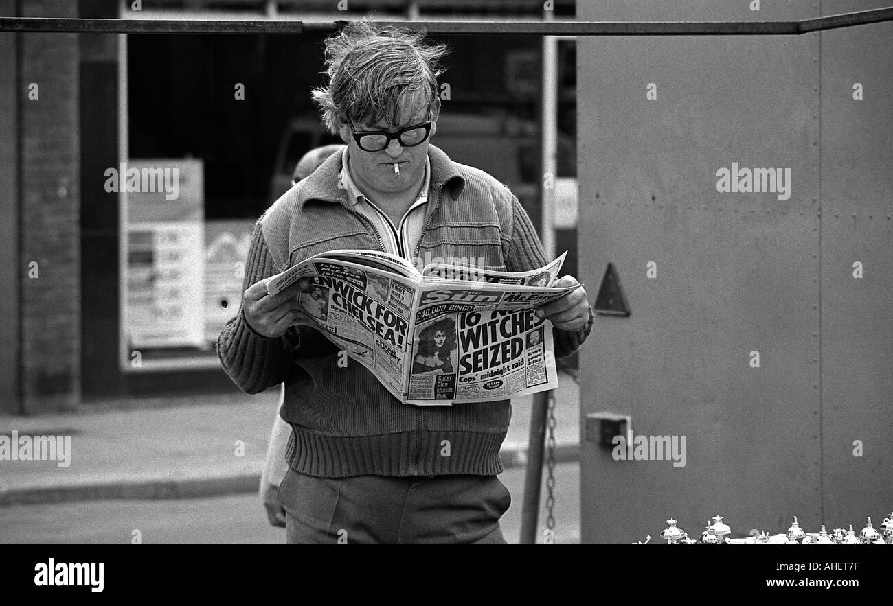 Uomo che cammina e la lettura del quotidiano Sun Foto Stock