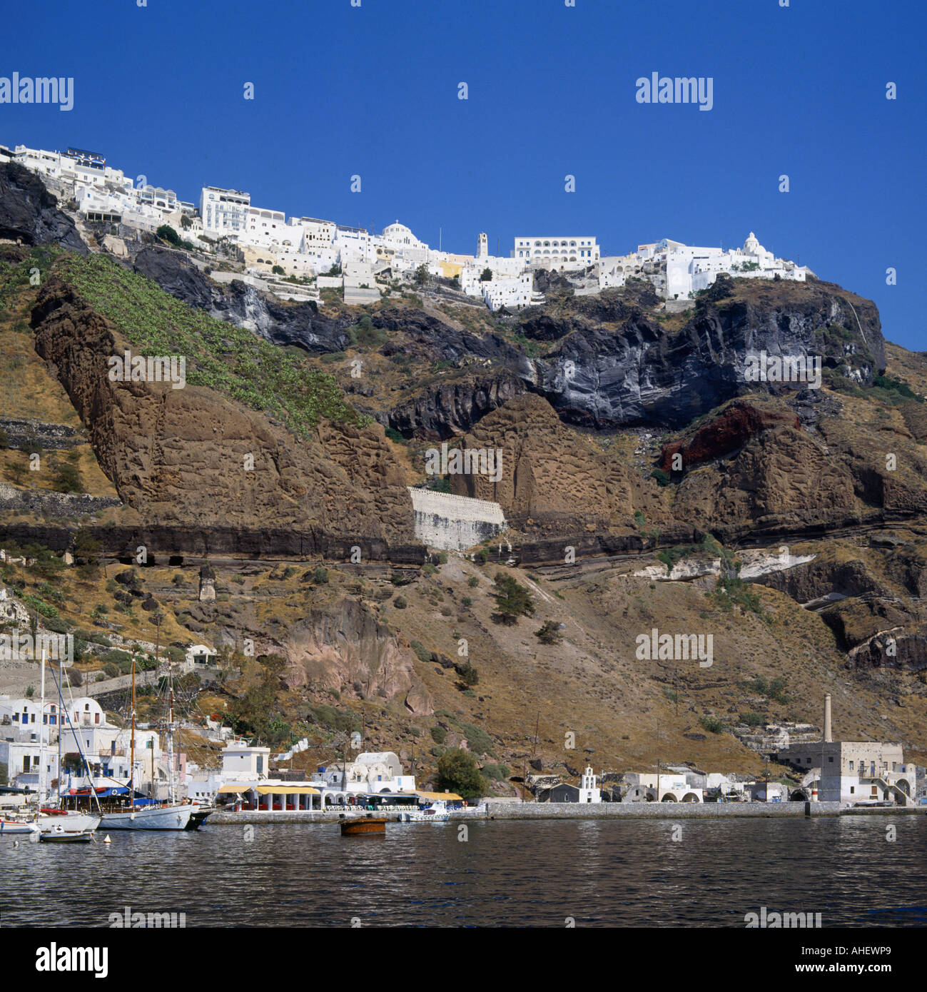 Vista attraverso acqua a ripide scogliere con edifici di colore bianco sulla parte superiore e un piccolo porticciolo al di sotto di Fira a Santorini Isole greche Foto Stock