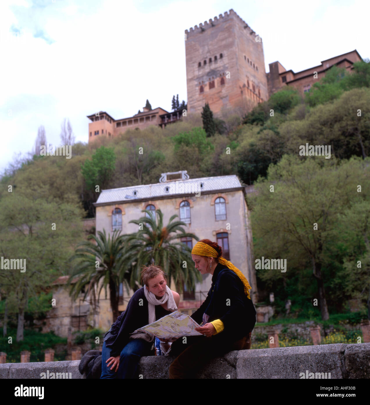 Giovani donne amici seduti su un muro vicino al fiume Douro con una vista della Alhambra Palace Mappa lettura in Granada Andalusia Spagna UE KATHY DEWITT Foto Stock