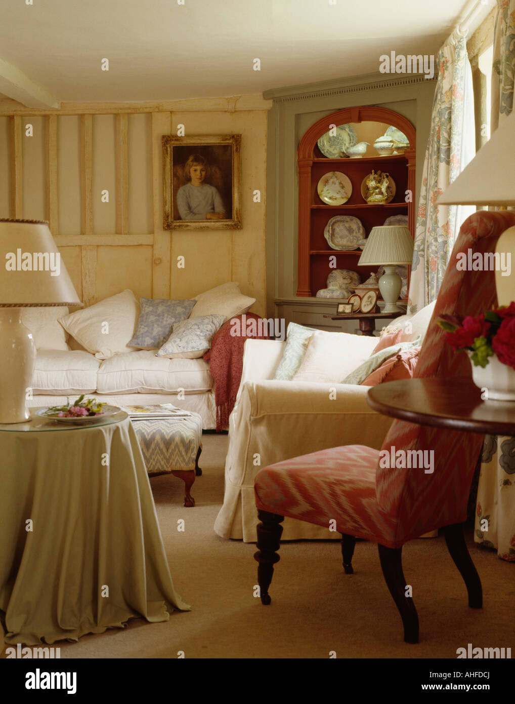 La crema divano e poltrona in cottage ingombra soggiorno con foto sulla parete accanto all antica angoliera Foto Stock