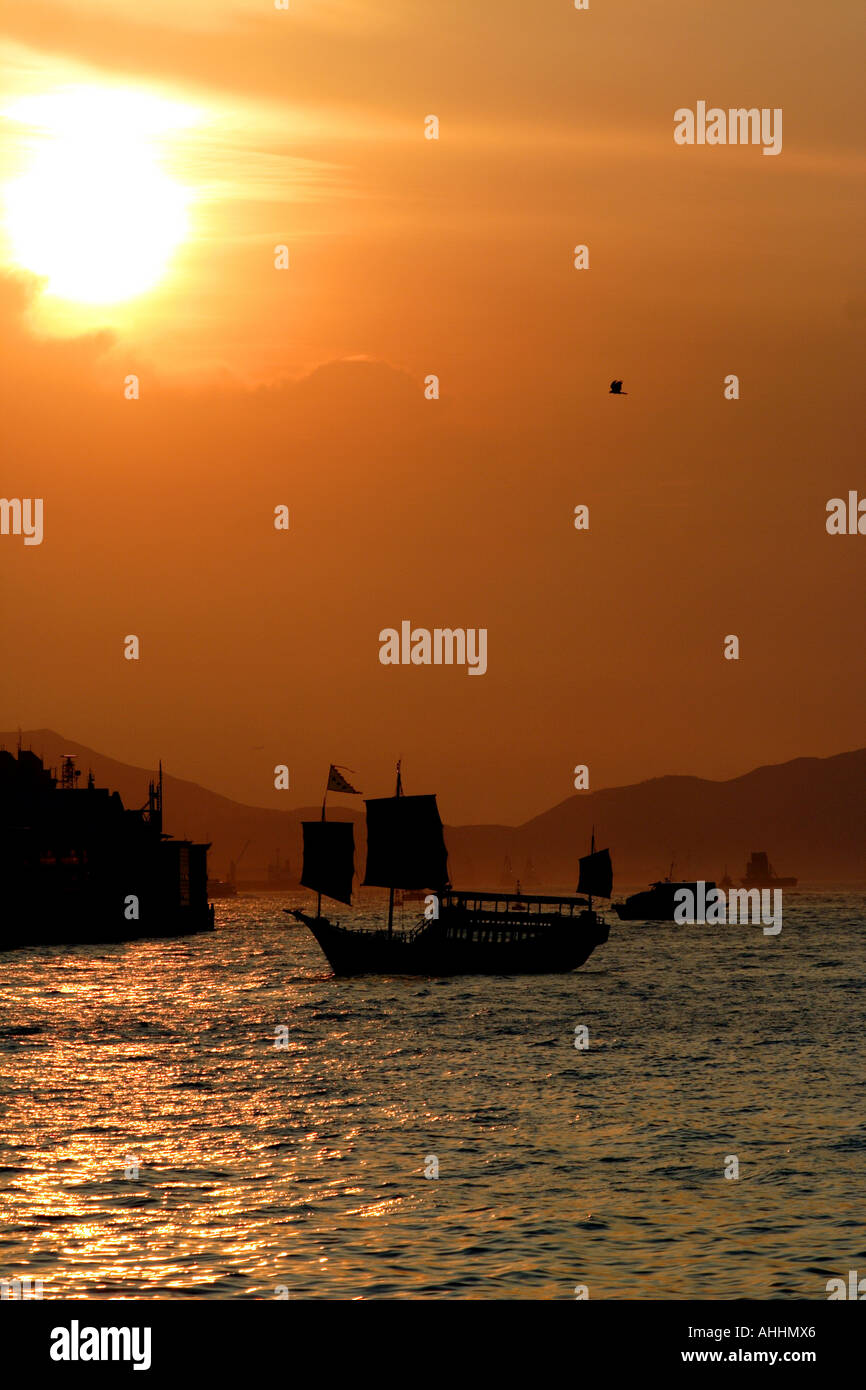 Vecchio giunca cinese di fronte a un dorato rosso tramonto nel porto di Victoria e di Hong Kong Foto Stock