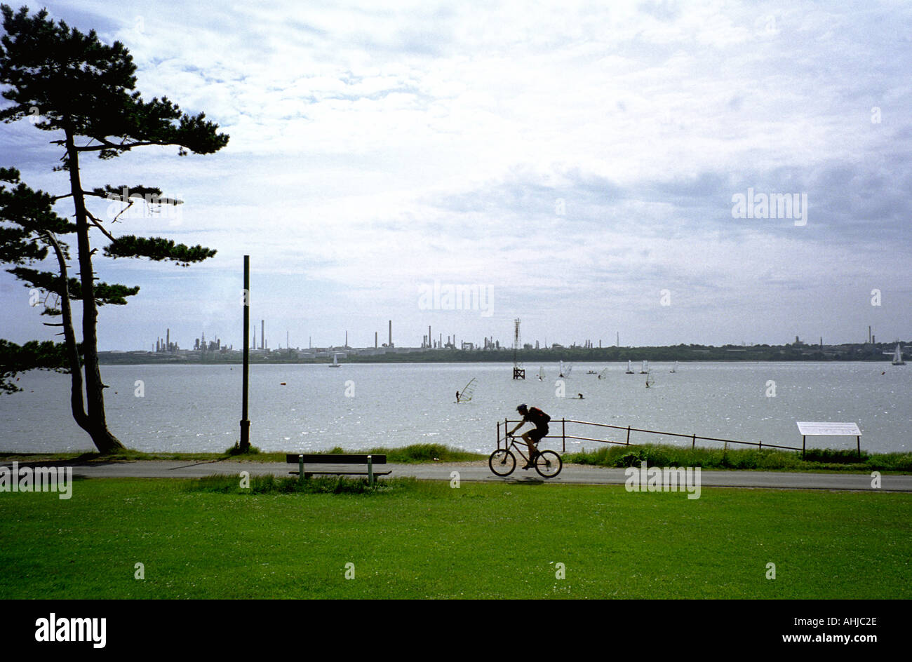 L'uomo pedalò lungo il sentiero accanto all'acqua di Southampton con windsurf e gommoni sulla raffineria di acqua e petrolio di Hythe Behind. Netley, Hampshire, Regno Unito. Foto Stock