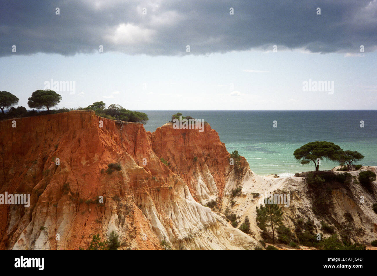 Vivace roccia di arenaria rossa con piccoli alberi in cima e blu mare verde dietro sotto il cielo di luna. Praia da Falesia, Algarve, Portogallo. Foto Stock
