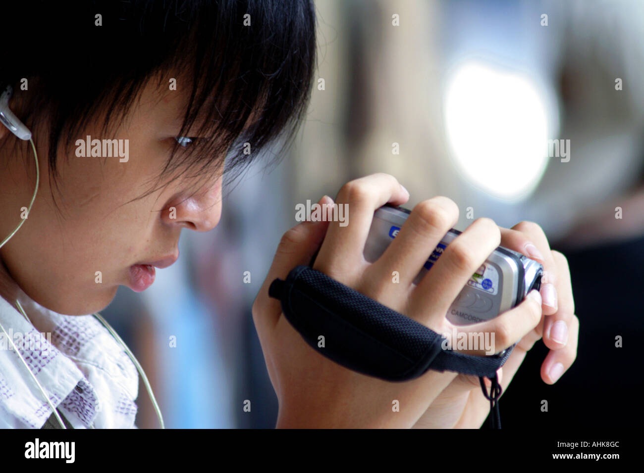 Asian adolescente che indossa le cuffie e utilizzando una videocamera digitale, registratore video Foto Stock