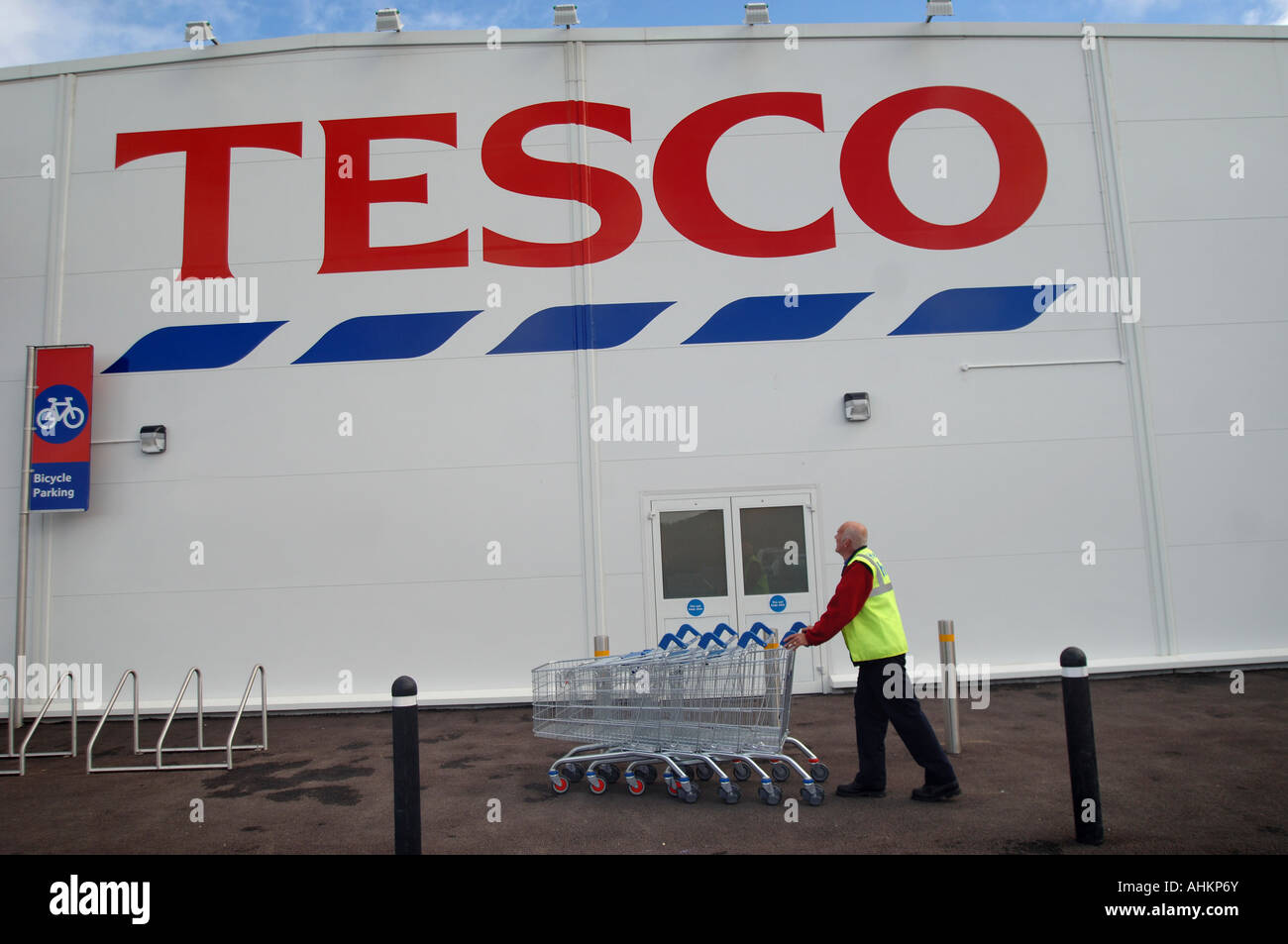 Un dipendente spinge un carrello passato un supermercato largeTesco superstore sign in Ilfracombe, North Devon, Regno Unito. Foto Stock