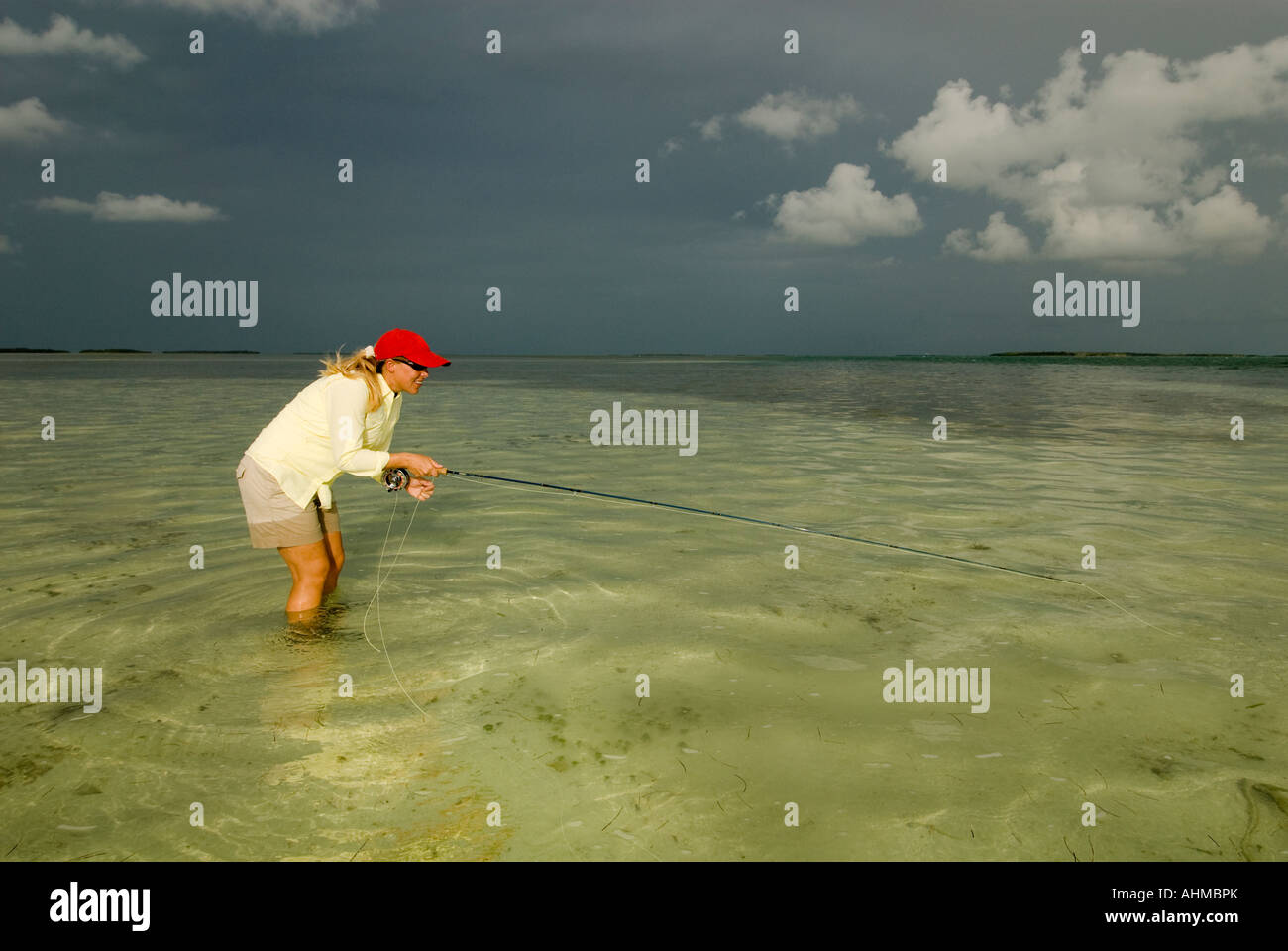 Florida Keys donna pescatore per colata Bonefish mentre la pesca con la mosca sotto cieli bui sulle parti piatte dell'oceano dei Caraibi Foto Stock